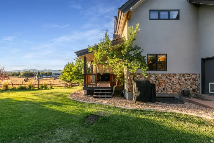 Expansive lawn with a stone and wood privacy fence, featuring a covered deck with wood flooring and built-in steps