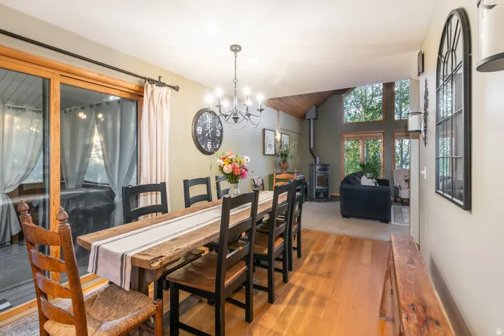 Hardwood flooring, wood-clad sliding glass door, exposed beam vaulted ceiling, freestanding wood-burning stove, and a decorative chandelier