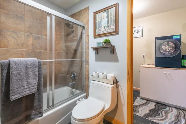 Bathtub with sliding glass enclosure, brown tile surround, and chrome fixtures