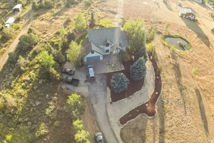 Gable roof residence with an attached garage, featuring a paved driveway, landscaped planting beds with mature trees, and an on-property pond