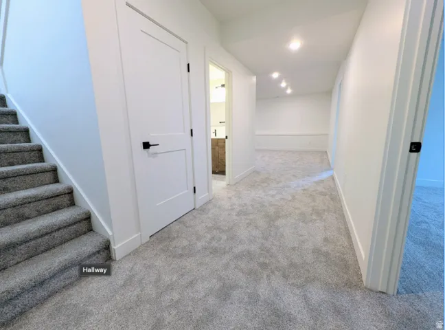 Plush gray carpeting throughout, featuring white interior doors with matte black hardware, recessed ceiling lighting, and a carpeted staircase
