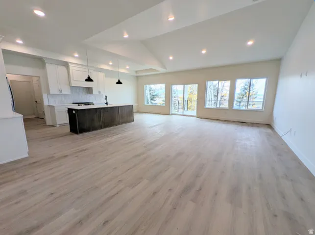 Open-concept living area featuring light wood-finish flooring, a kitchen island with a dark wood-finish base and light countertop, and a white tile backsplash