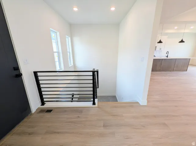 Light wood-finish flooring, contemporary black metal stair railing, high ceilings, recessed lighting, and a modern kitchen island with pendant lighting