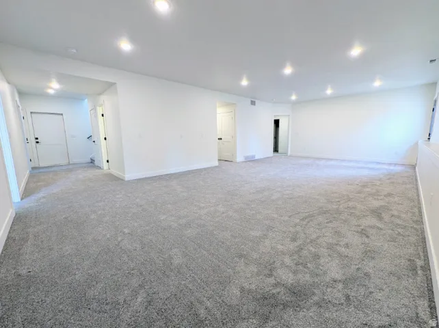 Expansive room featuring plush gray carpeting, recessed ceiling lighting, and crisp white walls