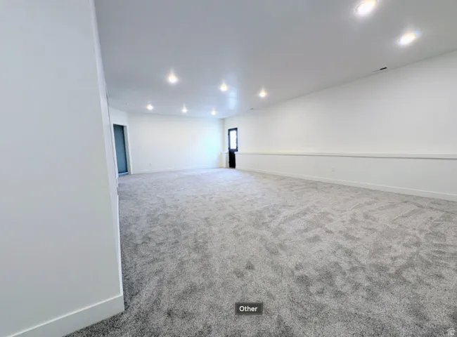 Expansive room featuring plush gray carpeting, recessed ceiling lighting, and crisp white walls with wainscoting