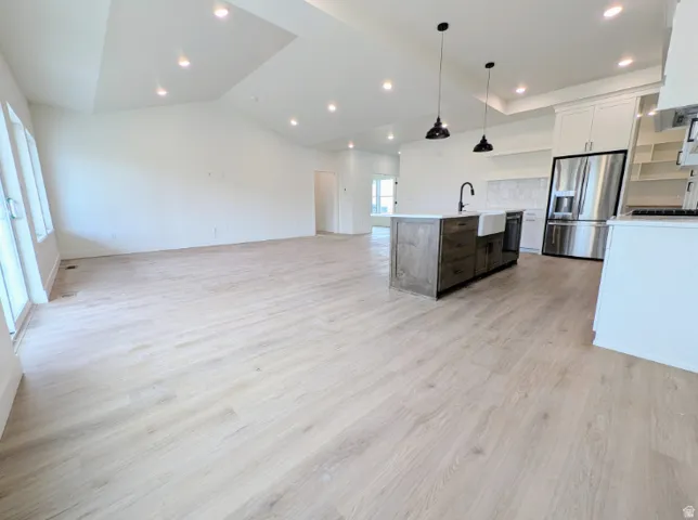 Vaulted ceilings with recessed lighting, wood-finish flooring, kitchen island with farmhouse sink, stainless steel refrigerator, and white cabinetry