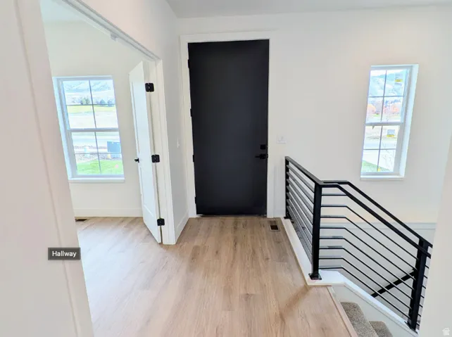Hallway featuring wood-finish flooring, a contemporary black door, and a staircase with a horizontal metal railing