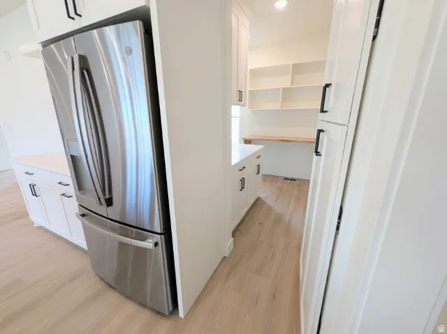 Stainless steel French door refrigerator, white cabinetry with black hardware, light-toned wood-finish flooring, and white countertops