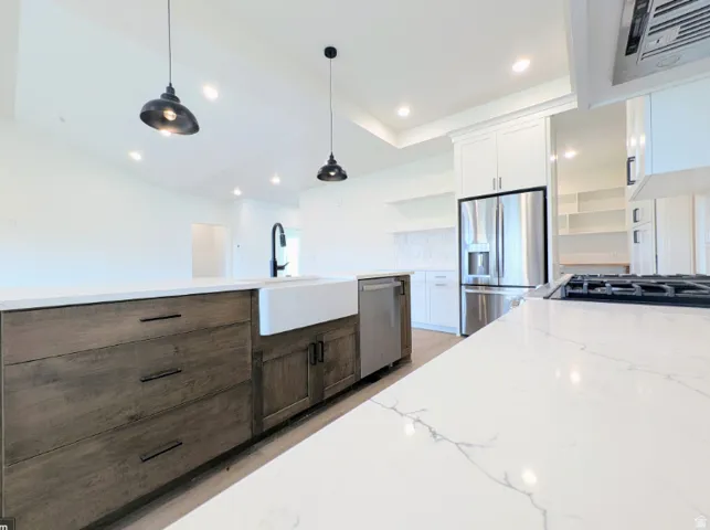 Kitchen featuring an oversized island with a farmhouse sink, stainless steel appliances, white cabinetry, and recessed lighting