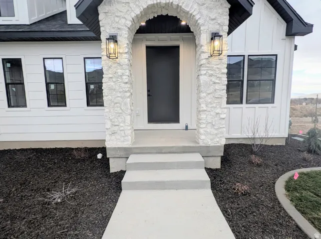 Arched stone entryway featuring a dark-paneled door, black-framed windows, and exterior sconces