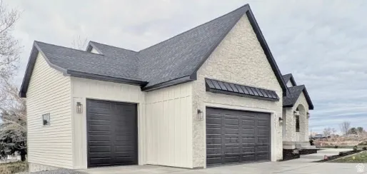 Property exterior featuring a multi-gabled roofline, two black garage doors, board and batten siding, and stucco finishes