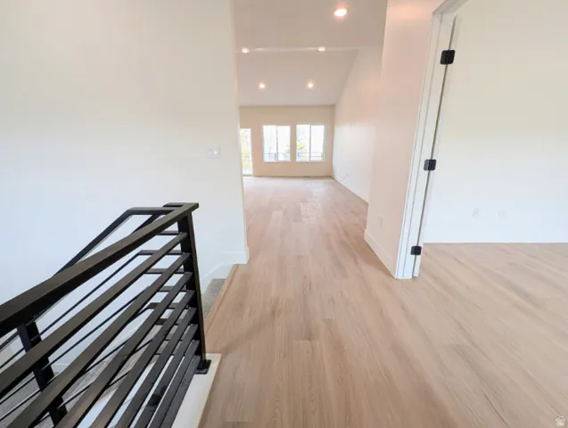 Wood-finish flooring throughout, vaulted ceiling, recessed lighting, and a contemporary black metal stair railing
