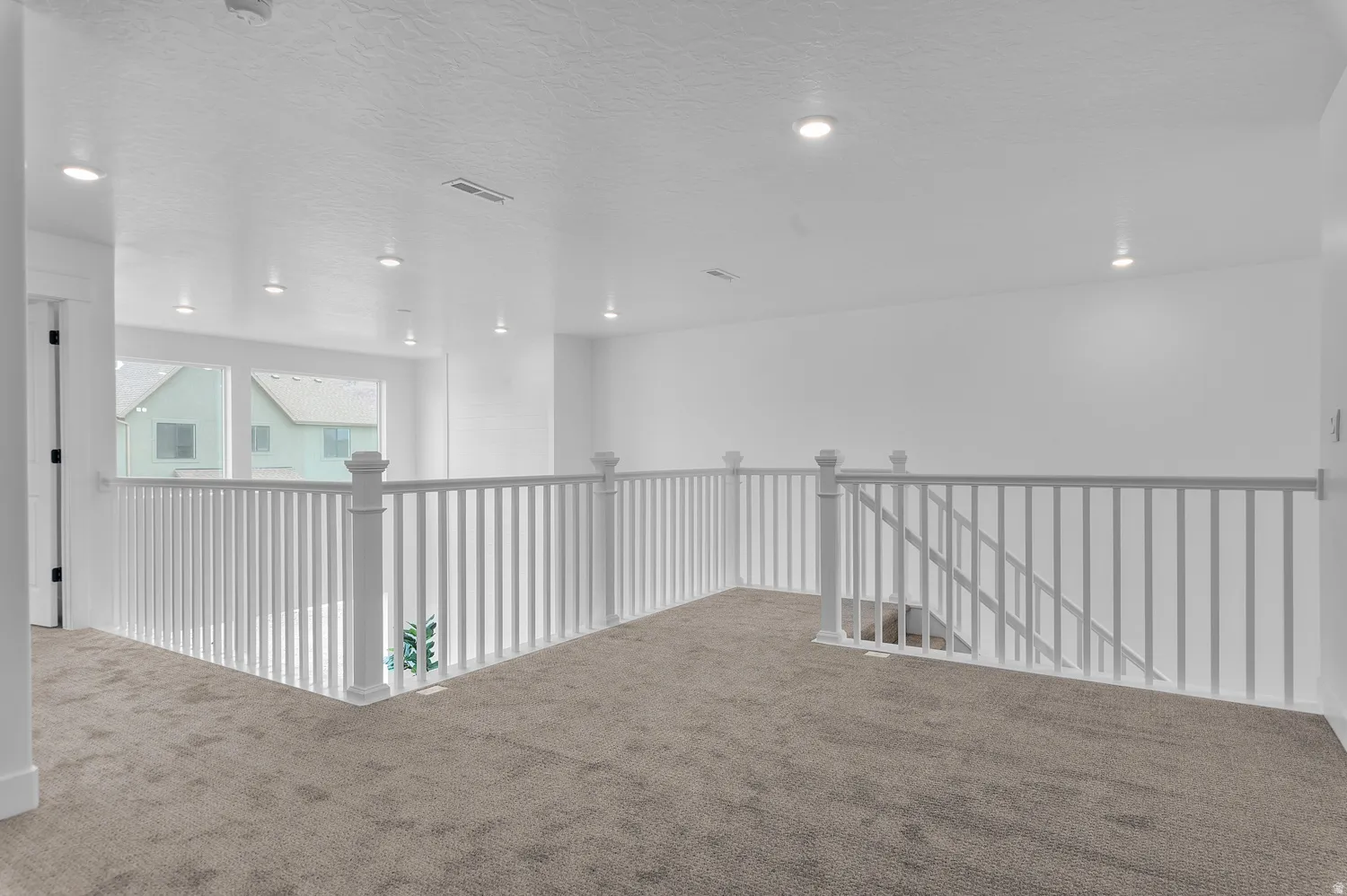 Carpeted loft space featuring white painted walls, recessed lighting, and a white balustrade railing