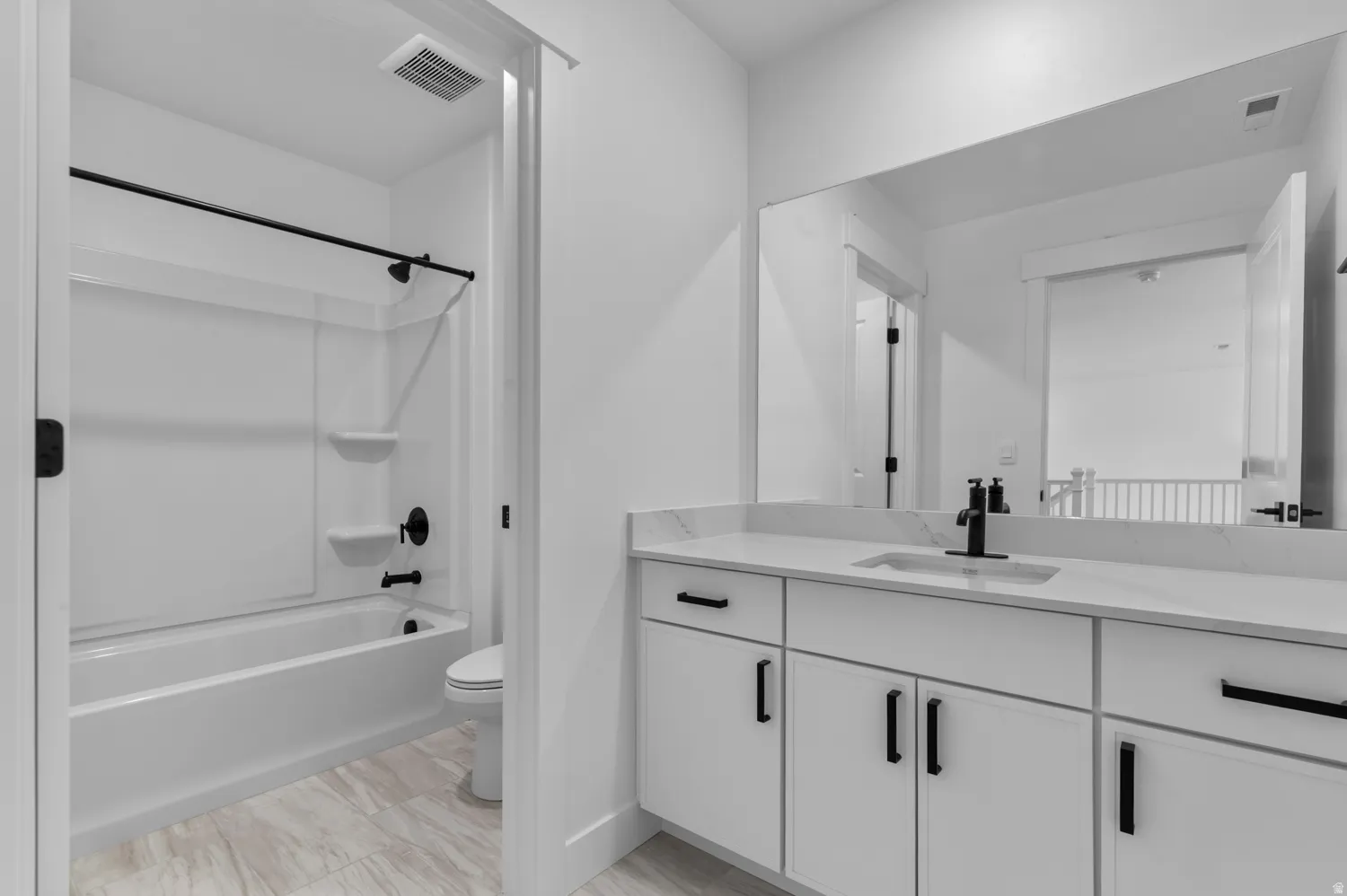 Bathroom featuring a white vanity with black hardware, a single rectangular sink, a large wall-mounted mirror, and a white tub with a shower and black fixtures