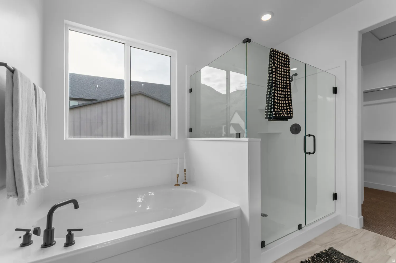 Spacious soaking tub with matte black fixtures, an expansive glass-enclosed shower, and a large window
