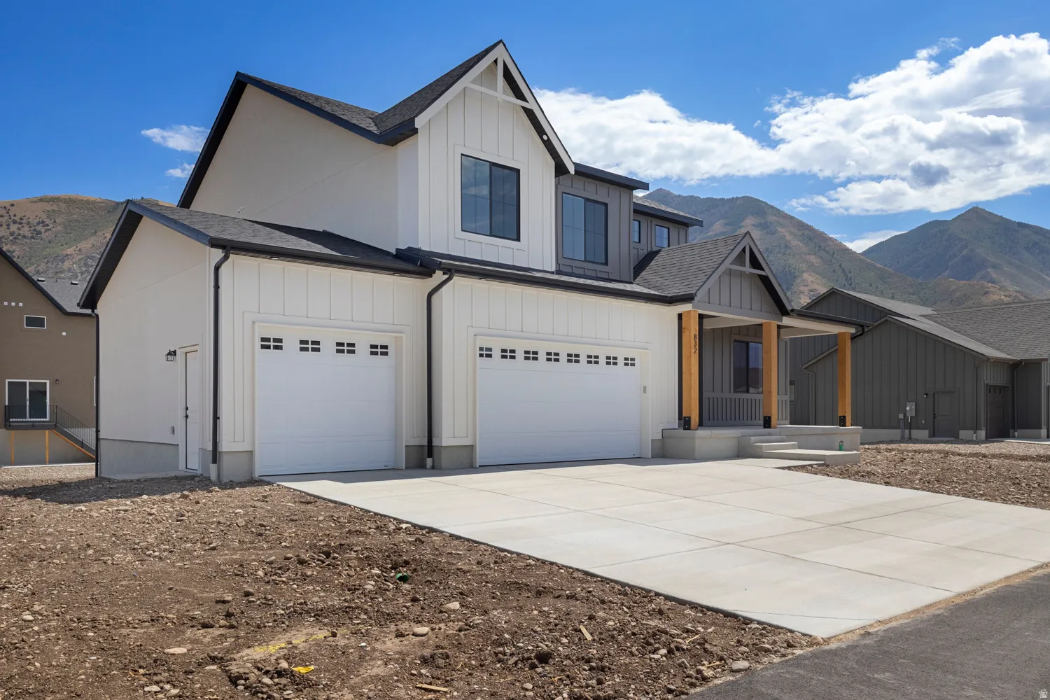 Modern farmhouse exterior featuring board and batten siding, a covered entry with wood posts, and a multi-car garage with panel doors