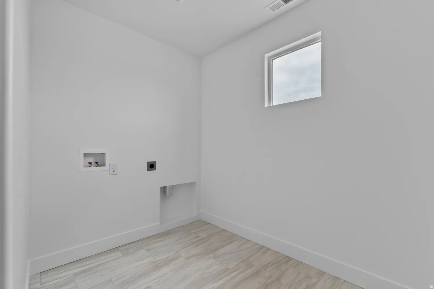 Laundry area featuring wood-finish flooring, a window, and utility connections