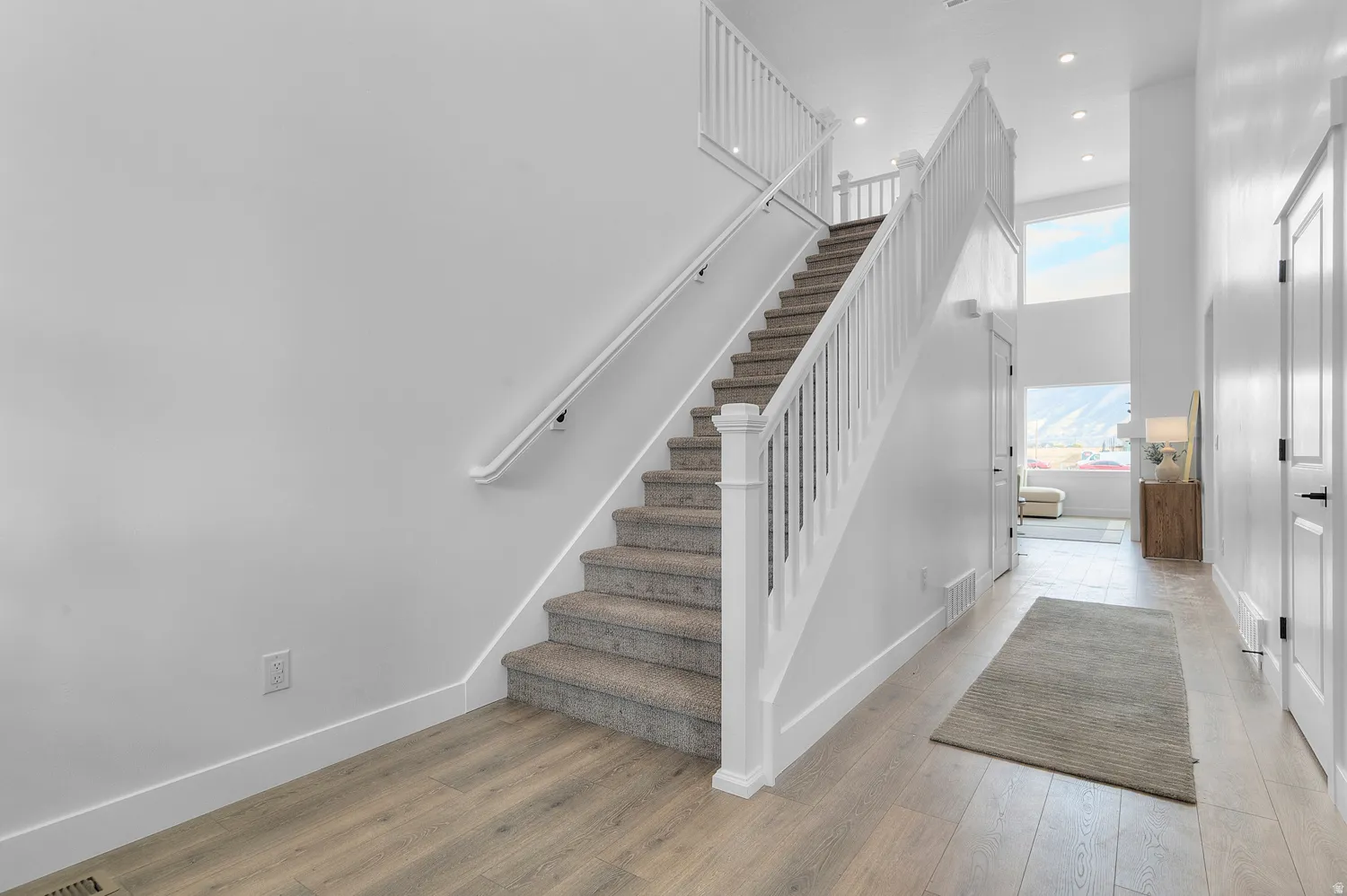 Two-story entryway with wood-finish flooring, a carpeted staircase with white railings, and tall windows