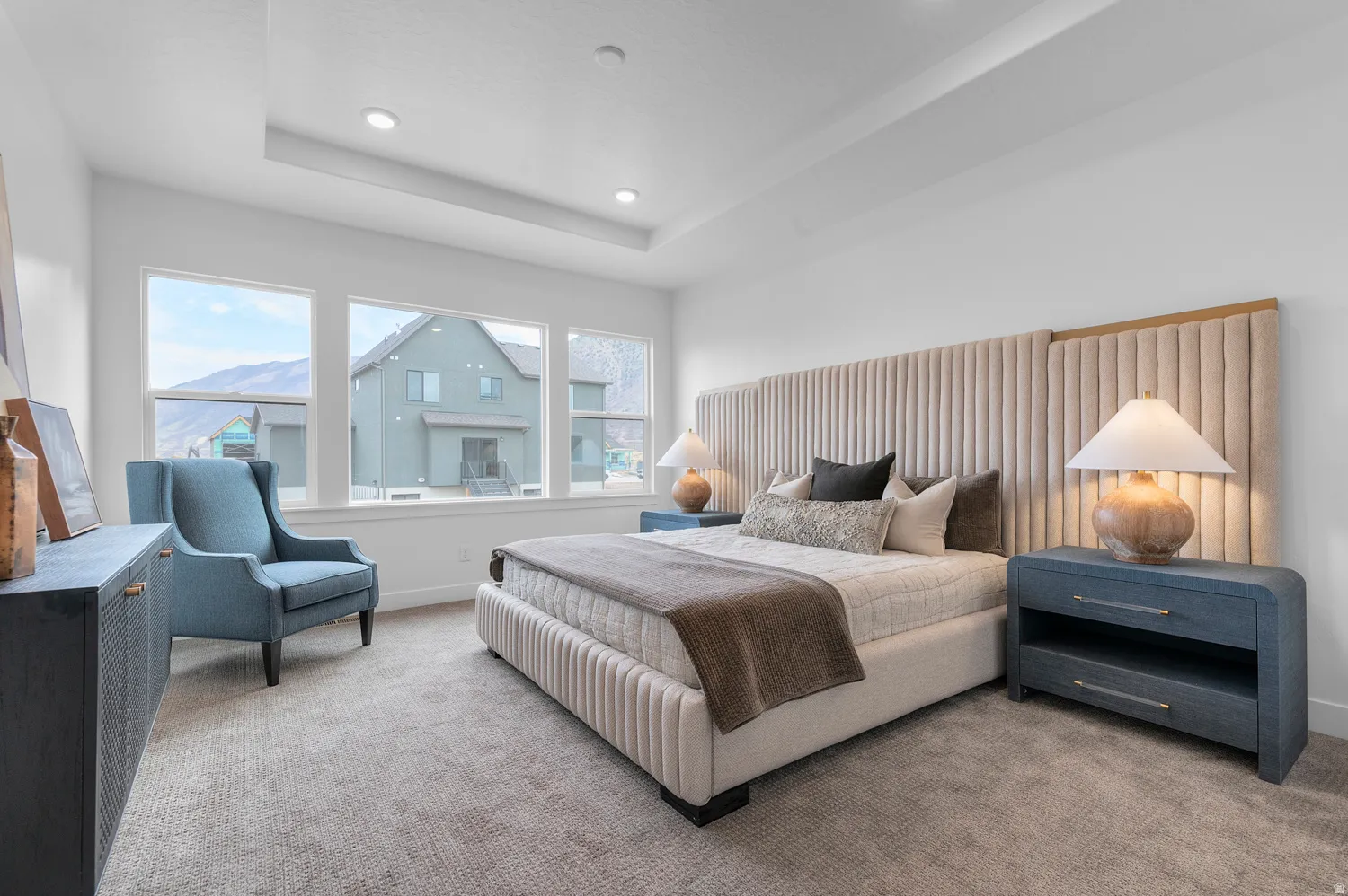 Recessed lighting, large windows, tray ceiling, upholstered bed frame, and soft carpet flooring