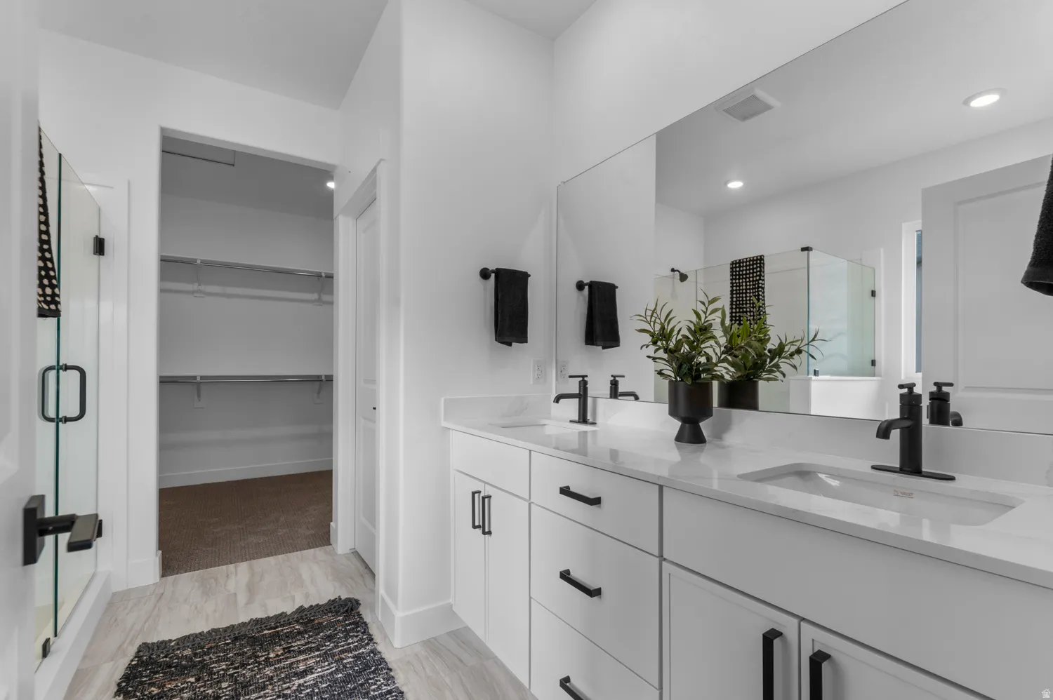 Dual vanity with white cabinetry and integrated sinks, a large wall-mounted mirror, and a glass-enclosed shower