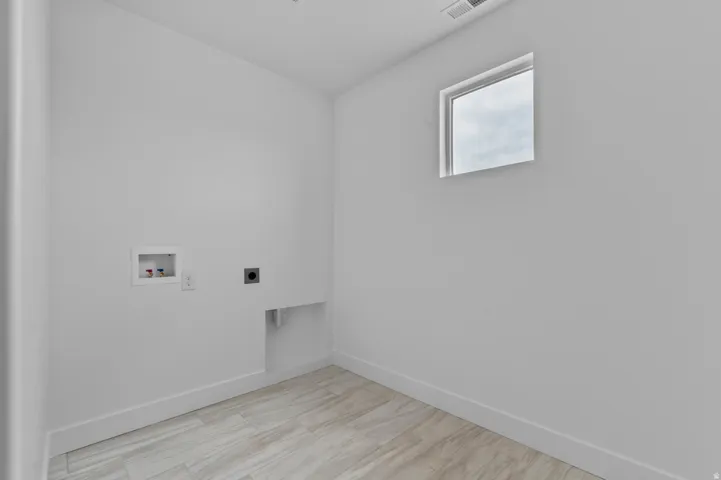 Laundry area featuring wood-finish flooring, a window, and utility connections