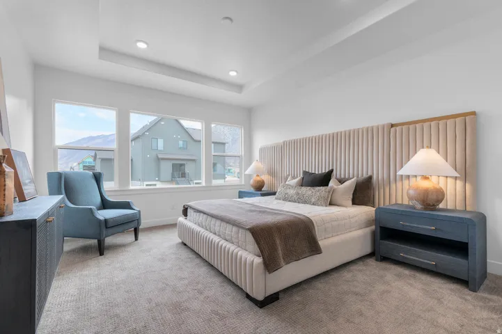 Recessed lighting, large windows, tray ceiling, upholstered bed frame, and soft carpet flooring