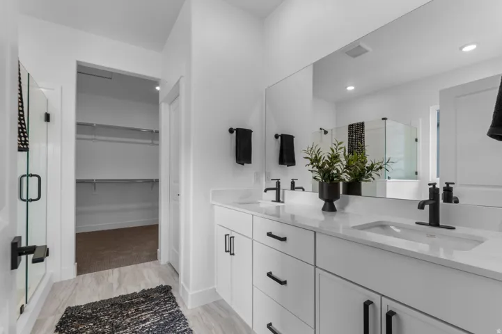 Dual vanity with white cabinetry and integrated sinks, a large wall-mounted mirror, and a glass-enclosed shower