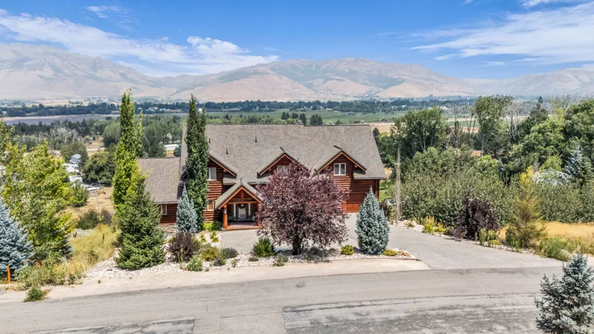 Log-style exterior with gabled roofline, mature landscaping, paved driveway, and mountain scenery