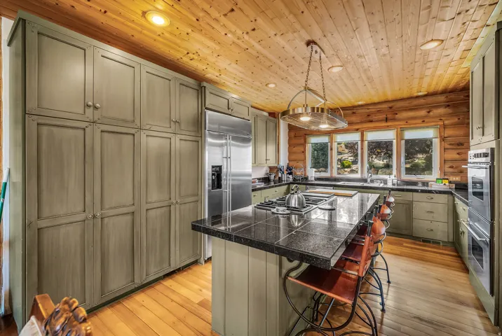 Kitchen featuring wood-finish flooring, full-height cabinetry, a large kitchen island with cooktop, and built-in stainless steel appliances