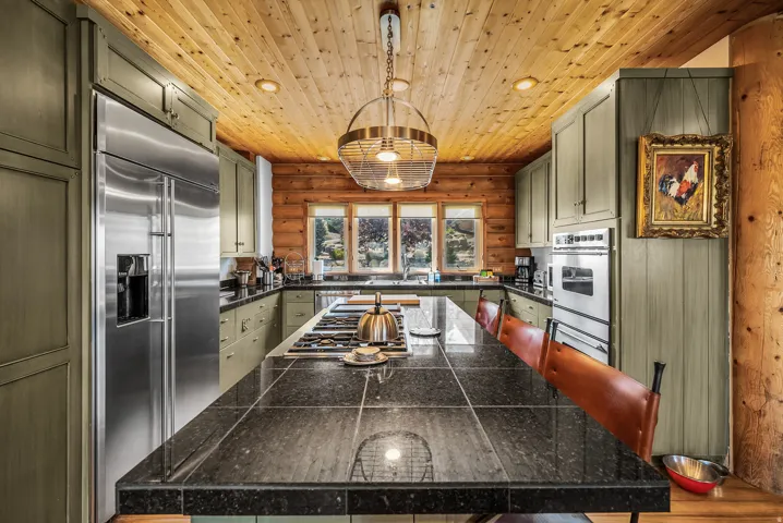Kitchen featuring log walls, wood-paneled ceiling, recessed lighting, and a large center island with a cooktop