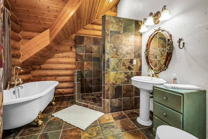 Slated shower enclosure with matching flooring, pedestal sink, and freestanding clawfoot tub