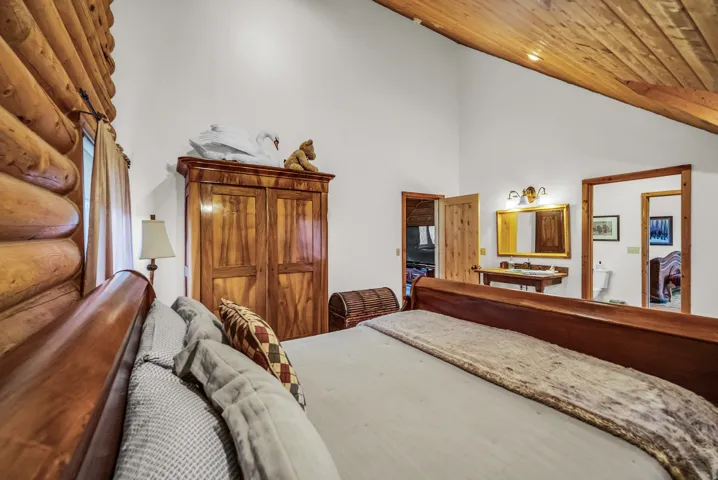 Exposed log wall, vaulted wood-finish ceiling, wood-finish doors, wood-finish vanity with basin sink, and wall-mounted vanity lighting