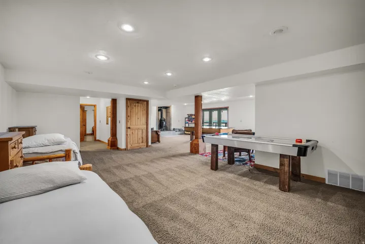 Carpeted open-concept room with recessed lighting, exposed wood support beam, and natural wood doors