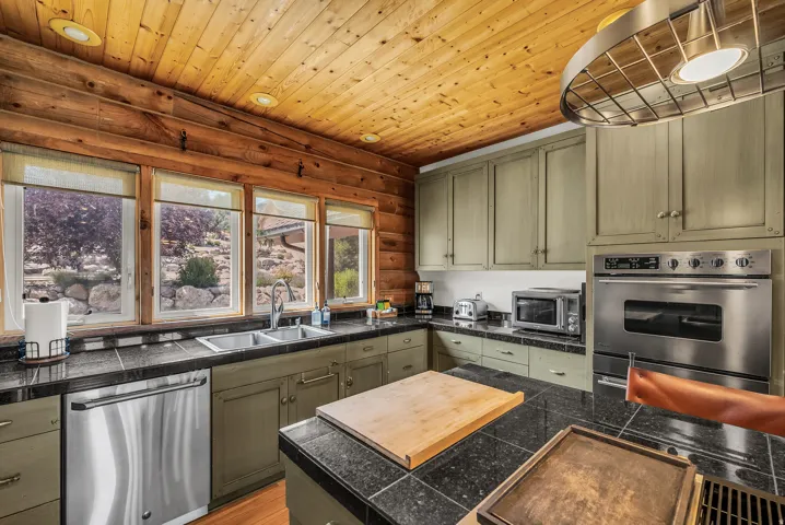 Kitchen featuring a wood plank ceiling, log walls, dark countertops, built-in stainless steel oven, and green cabinetry
