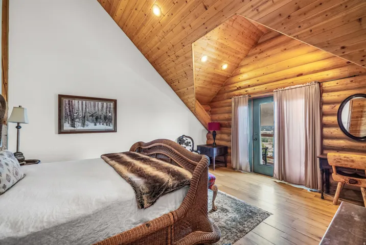 Wood-finish flooring, vaulted wood-paneled ceiling, exposed log wall, white wall finish, and a glass-paneled door