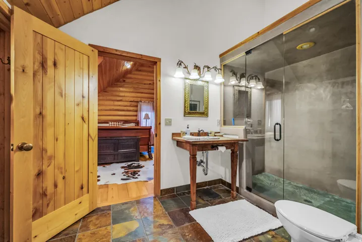 Wood-paneled door, slate-tile flooring, glass-enclosed shower, wood vanity with basin sink, and wood-paneled ceiling