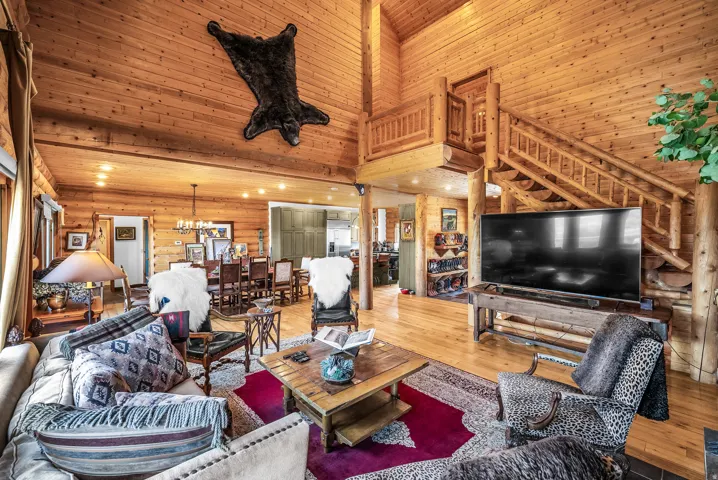 Vaulted wood-paneled ceiling, exposed log beam construction, open concept living area, wood flooring, and a built-in wood staircase with a landing