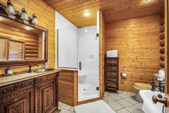 Wood-paneled bathroom featuring a glass-enclosed shower, carved wood vanity with a vessel sink, and ceramic tile flooring