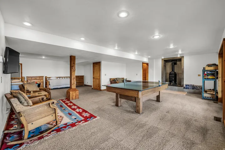 Carpeted lower-level room featuring recessed lighting, a wood-burning stove with stone surround, and wood-paneled doors