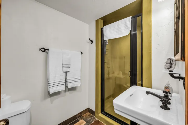 Walk-in shower with a black-framed glass enclosure, pedestal sink with dark bronze fixtures, and natural stone tile flooring