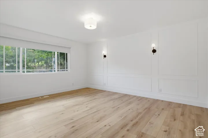 Another shot of the main bedroom with wood-finish flooring, accent wall with panel molding, two wall-mounted sconces, recessed window, and flush mount lighting