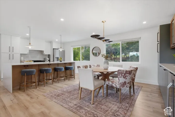 Open-concept kitchen and dining area featuring a kitchen island with seating, stainless steel appliances, wood-finish flooring, and multiple large windows
