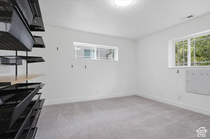 Den/office or bedroom down with built-in shelving system with mesh baskets, two windows, recessed ceiling light, and light gray carpeting