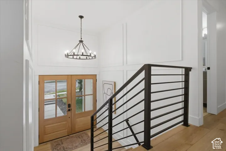 Double wood-paneled entry doors with glass panels, wrought iron chandelier, paneled accent wall, wood-finish flooring, and a contemporary metal staircase railing