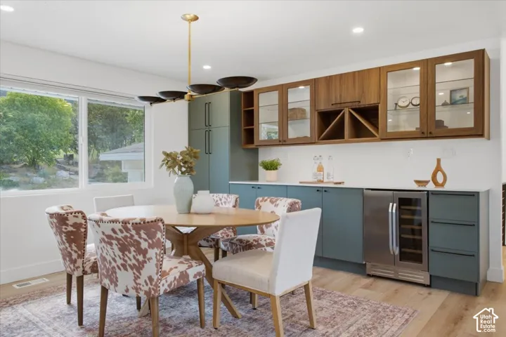 Integrated dining area featuring a modern chandelier, abundant natural light from large windows, wood-finish flooring, built-in extra cabinetry, and a beverage cooler