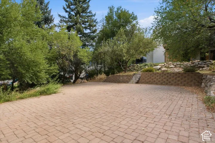 Brick paver surface, stone retaining walls, mature trees, and natural landscaping