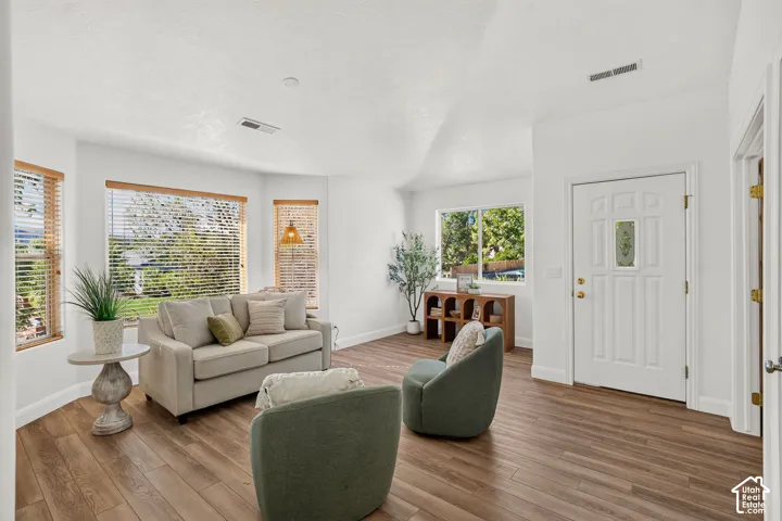 Wood-finish flooring throughout, multiple windows with natural wood trim, white paneled entry door with decorative glass insert, and recessed ceiling lighting
