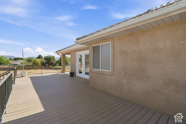 Expansive composite deck with black metal railings, stucco exterior, and white French doors