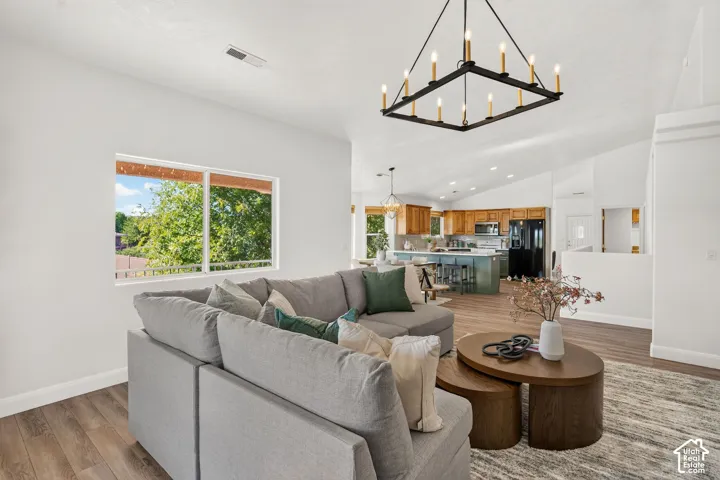 Vaulted ceilings, wood-finish flooring, a contemporary chandelier, and an open-concept layout