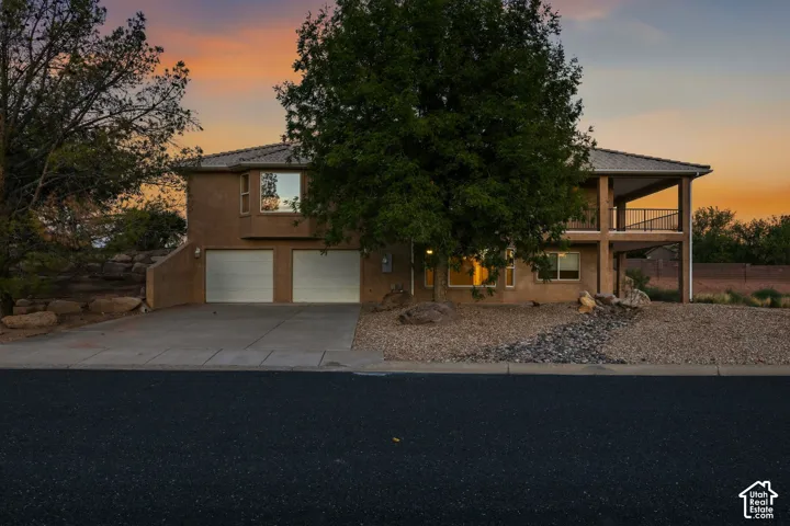 Two-story residence featuring a stucco exterior, an attached two-car garage, and an upper-level covered balcony with black railings